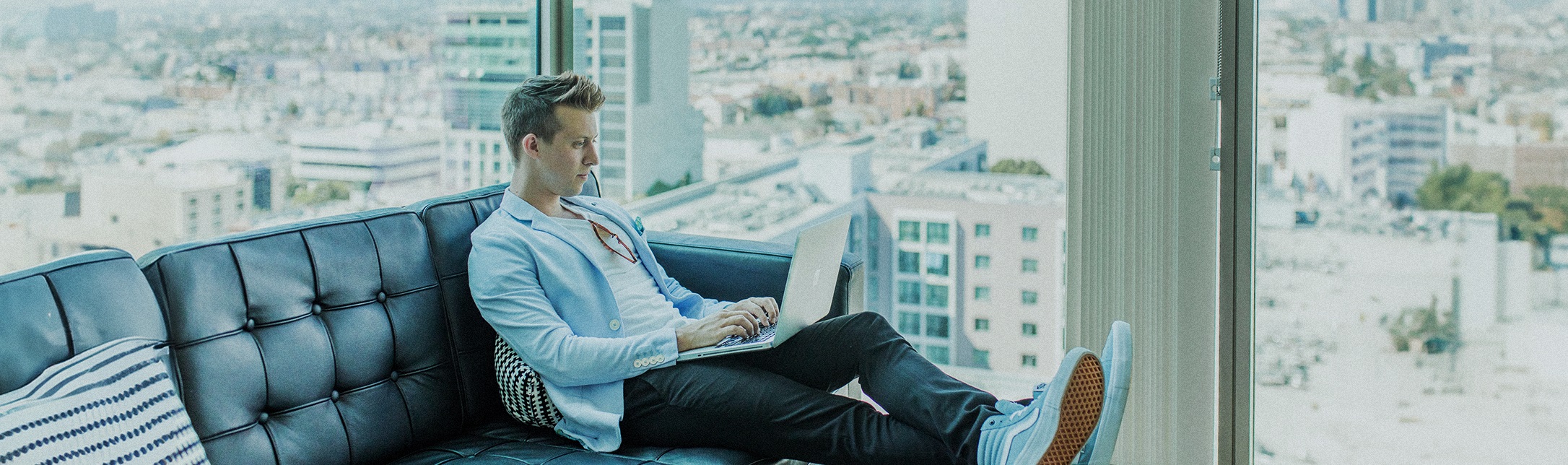 Ein Business Man sitzt in einem verglasten Büro mit hochgelegten Beinen und einem Laptop auf dem Schoß