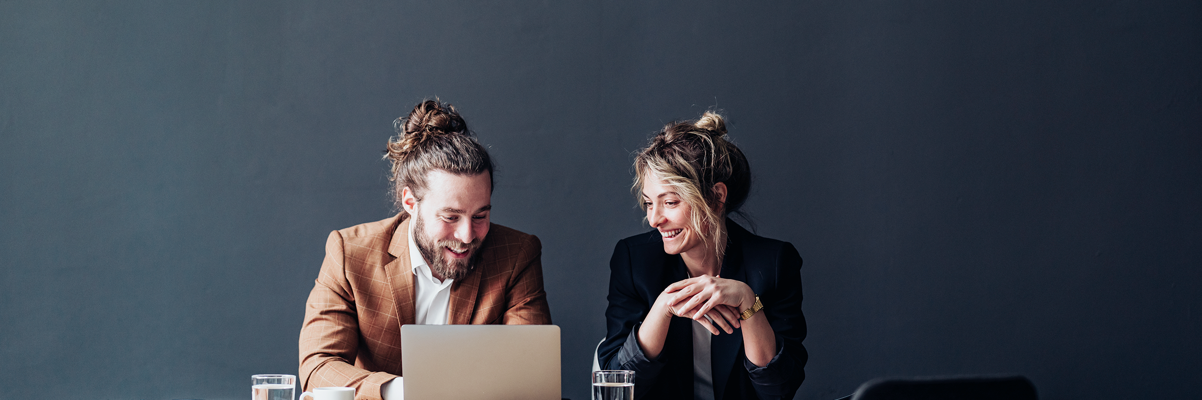 Ein Mann und eine Frau sitzen vor einem Laptop und lächeln
