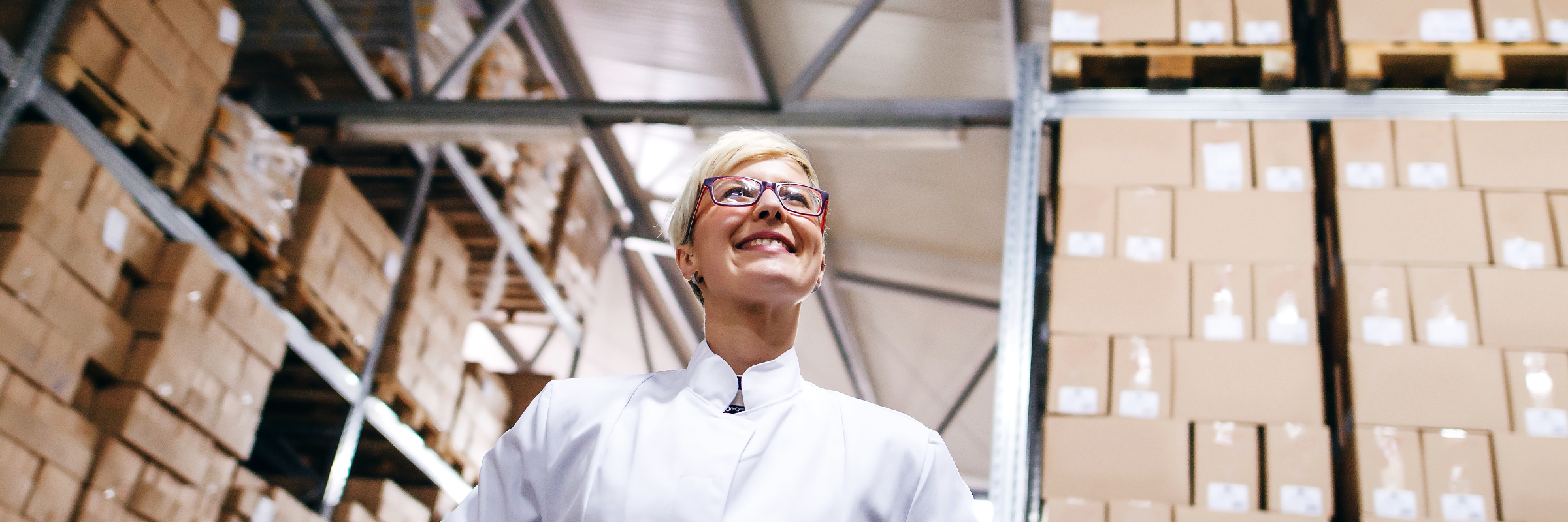 Eine Frau mit Brille steht lächelnd in einer Lagerhalle
