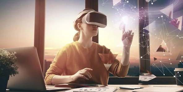 Eine Frau sitzt am Schreibtisch und hat eine AR/VR-Brille auf